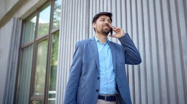 Gülümseyen işadamı modern ofis binasının dışında telefon görüşmesi yapıyor. İş ağı kavramı, liderlik, kariyer gelişimi ve profesyonel yaşam tarzı.