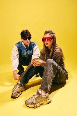 Büyük boy sokak kıyafetleri ve parlak sarı sette güneş gözlüğü takan havalı genç mankenler. Gençlik modası, sokak kıyafetleri, alt kültürler ve yaratıcı markalaşma kavramı.