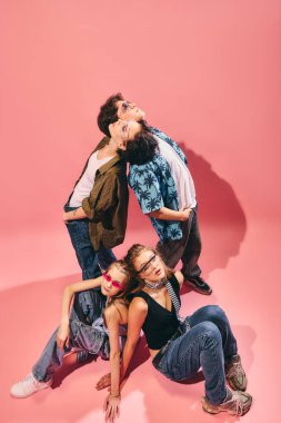 Pembe arka planda yaratıcı bir şekilde poz veren şık bir gençlik grubu. Gençlik modası kavramı, sokak kıyafetleri alt kültürleri, pop kültür makaleleri, festival tanıtımı, genel Z markası..