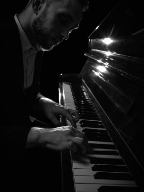 Dramatik, sade ışıklandırmada duygusal odaklı piyano çalan bir adam. Müzik performansı, yaratıcı tutku, konser tanıtımı, sanat eğitimi ve kültürel etkinlikler kavramı.