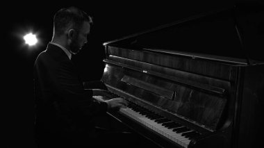 Karanlık atmosfer ortamında sahne ışığı altında piyano çalan bir piyanist. Sahne performansı, canlı müzik, kültürel etkinlikler, profesyonel sanatçılık ve yaratıcı promosyon kavramı.