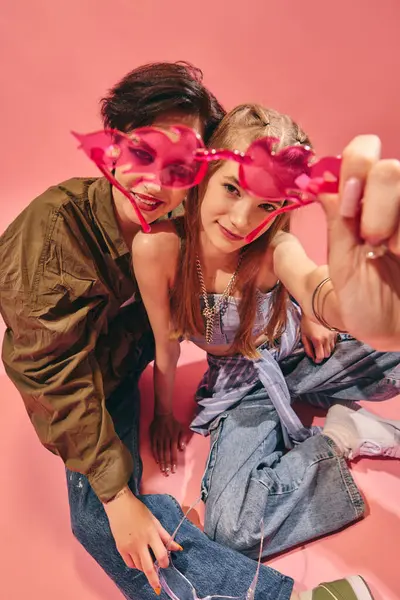 Pembe arka planda otururken pembe güneş gözlüğü gösteren şık arkadaşlar. Gençlik modası, sokak kıyafetleri kültürü, pop kültürü ve yaratıcı markalaşma kavramı.