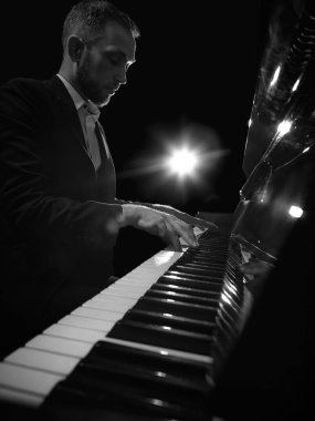 Dramatik sahne ışıkları altında derin duygusal odaklı piyano çalan bir adam. Müzik festivali posterleri, yayın kapakları, ses markası reklamları, farkındalık içeriği, piyano dersleri kavramı.