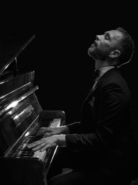 Smokinli bir adam karanlık sahnede gözleri kapalı piyano çalıyor. Müzik festivali posterleri, yayın kapakları, ses markası reklamları, farkındalık paylaşımları, piyano dersleri, müzik blogları kavramı