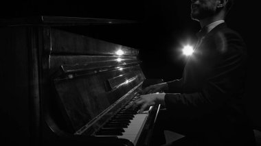 Smokinli bir adam karanlık sahnede piyano çalıyor ve sahne ışıkları enstrüman yüzeyine yansıyor. Müzik festivali posterleri, yayın kapakları, ses markası reklamları, piyano dersleri, müzik blogları kavramı.