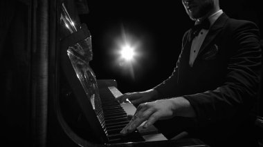 Erkek piyanistlerin elleri dramatik bir sahne ışığı altında odaklanmış ifadeyle piyano çalarken. Canlı müzik performansı, sanatsal tutku, konser atmosferi kavramı.