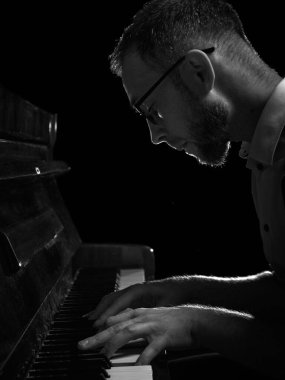 Gözlüklü, koyu renk tek renkli ışıkta piyano çalan bir adam. Müzik akademisi broşürü, konser tanıtımı, enstrüman eğitimi, kültürel etkinlik markalaşması, sanatsal yaşam tarzı içeriği kavramı.
