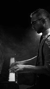 Arka planda ışık ve atmosferik dumanla piyano çalan bir adam. Dramatik konser sahnesi, sanatsal caz performansı, duygusal canlı müzik kavramı.
