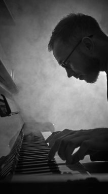 Yan görüntüdeki piyanist yoğun odaklanma ve dramatik dumanla piyano çalıyor. Sanatsal performans kavramı, müzik etkinliği markalaşması, caz tanıtımı, kültürel sahne sunumu.