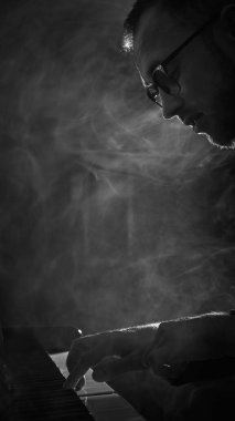 Duman etkisiyle karamsar monokromda piyano çalan piyanistin yan görüntüsü. Canlı performans, müzik fotoğrafçılığı, albüm kapakları, yaratıcı reklamcılık ve kültürel promosyon kavramı.