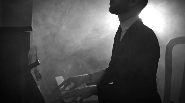 Takım elbiseli bir adam dramatik sahne ışıklarıyla piyano çalıyor. Canlı performans konsepti, klasik müzik, konser tanıtımı, kültürel etkinlikler, müzisyen markalaşması.