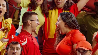 Kırmızı ve sarı tişörtlü iki taraftar maç sırasında yüz yüze bağırıyor. Duygusal reklamcılık kavramı, destek kültürü, spor markalaşması, çeşitlilik kampanyaları.