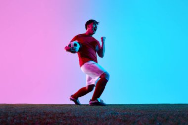 Sahada galibiyeti kutlayan heyecanlı futbolcu, topu elinde tutuyor. Duygusal başarı, spor zaferi ve profesyonel futbolda rekabetçi ruh kavramı..