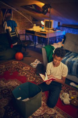 Çocuk desenli halıda kırmızı defter okuyor. Öğrenme ve hayal gücü kavramı, yaratıcı düşünce, gençlik gelişimi, ve huzurlu ve rahat bir iç mekanda odaklanma..