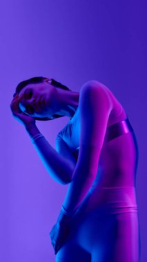 Sanatsal neon ışıklı kadın modası fütüristik zarafetle poz veriyor. Avant-garde fotoğrafçılık, duygusal içgözlem ve canlı mor-mavi gradyan ışıkta yüksek moda estetiği kavramı.