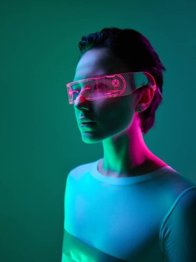 Yeşil arka planda pembe ve siber ışık saçan neon ışıklı bir kadın. Gelecekçi moda, siber tarz ve cesur bireysellik kavramı.
