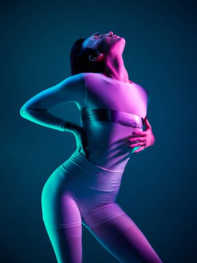 Beyaz elbiseli bir kadın dramatik Cyan ve eflatun ışıkların altında sırtını kamburlaştırıyor. Gelecekçi tarz kavramı, vücut ifadesi, güçlendirme ve duygusal yoğunluk..