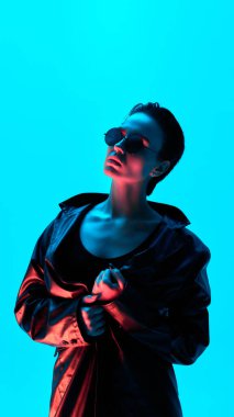 Siberpunk 'tan esinlenilmiş deri gibi poz veren kendine güvenen bir kadın. Gelecekçi stil kavramı, iddialı zarafet ve kendini ifade etme kalın neon mavi ve kırmızı ışıkta..