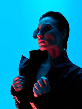 Deri ceketli ve neon ışıklı çarpıcı bir kadın. Öncü moda kavramı, güçlü karakter ve yoğun renk kontrastı altında korkusuz bireysellik..