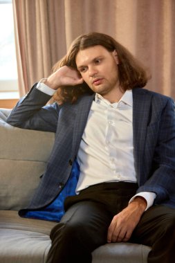 Takım elbiseli genç adam düşünceli bir tavırla kanepede oturuyor. Yansıma, yaşam tarzı, iş stresi, karar verme, profesyonellik ve güçlendirme kavramı.