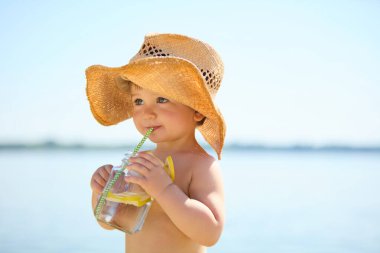 Hasır şapkalı çocuk sahilde samanla limonata içiyor. Yaz tatili kavramı, ferahlama, masumiyet, çocukluk keyfi, sağlık, su ve rahatlık..