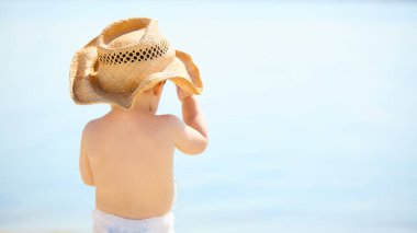 Hasır şapkalı çocuk huzurlu bir şekilde denize bakıyor. Çocukluk masumiyeti, yaz tatili, rahatlama, özgürlük, doğa bağlantısı ve tasasız yaşam tarzı kavramı..