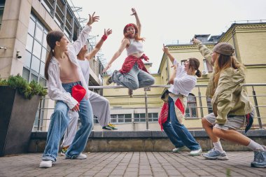 Kızıl saçlı sokak dansçısı tutkuyla yükselirken grup şehir ortamında tezahürat yapıyor. Gençlik kültürü, dans ve müzik kavramı, yaşam tarzı enerjisi, moda markalaşması ve sosyal medya içeriği.