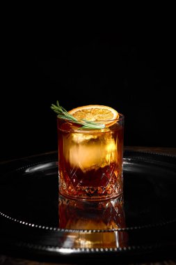 Portakal dilimli eski moda kokteyl ve yansıtıcı siyah tepside biberiye. Sanatçılık kavramı, bar kültürü, birinci sınıf zevk, kutlama ve miksoloji sanatı.