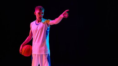 Beyaz formalı kızgın basketbolcu topu tutuyor ve neon ışığın altında işaret ediyor. Rekabet, liderlik, motivasyon ve spor markalaşması kavramı.
