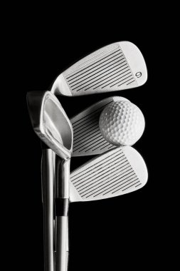 Three golf irons with ball balanced on clubface against dark background. Concept of sports precision, equipment showcase, advertising visuals and performance branding campaigns.