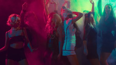 Young people dancing in colorful neon smoke during Halloween party celebration. Concept of entertainment, holiday advertising, youth emotions, nightlife and digital culture.