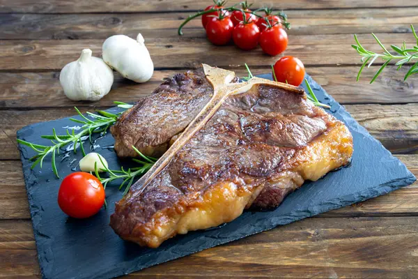 Kızartma tavasında biftek, kiraz domatesli, sarımsaklı ve biberiyeli ahşap masa.