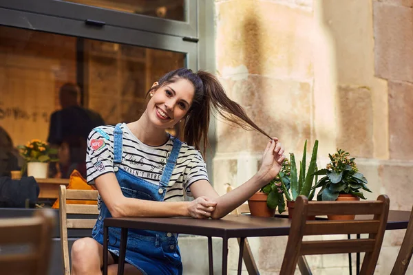 Kobieta Siedząca Kawiarni Zewnątrz Trzymająca Kucyk Patrząca Uśmiechniętą Kamerę — Zdjęcie stockowe