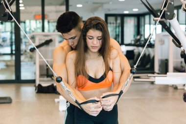 Genç bir adam kızın spor salonunda makine kullanmasına yardım ediyor..