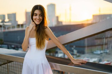 Arka planda gün batımı olan beyaz bir elbise giyen genç bir kadını vurdu..