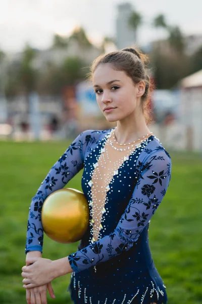 Młoda Gimnastyczka Kolorowym Niebieskim Garniturze Trzymająca Złotą Kulę Patrzącą Kamerę — Zdjęcie stockowe