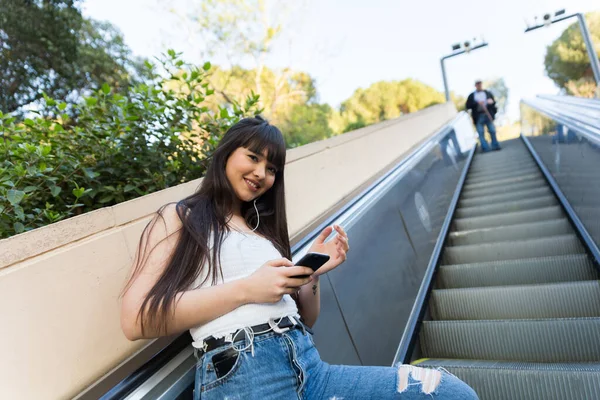 在巴塞罗那街道的自然光下 当她用手机和耳机听音乐时 一位亚裔欧裔妇女走在楼梯上 — 图库照片