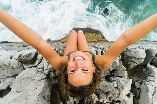 カメラを見上げ崖の端に座っている若いブロンドの女性の上から撮影 — ストック写真