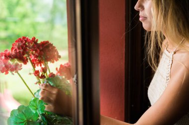Kırmızı bir bitkiye camdan dokunan tanınmayan genç bir kadın.