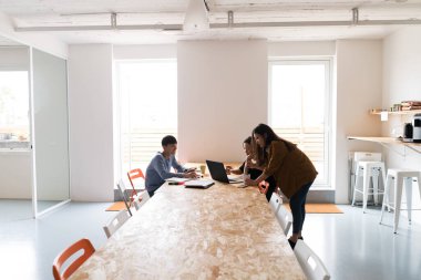 Masada oturan ve dizüstü bilgisayar ve kağıt belgeleriyle çalışan gençlerin yan görünümü.