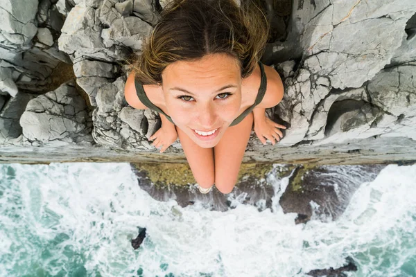 カメラを見上げ崖の端に座っている若いブロンドの女性の上から撮影 — ストック写真