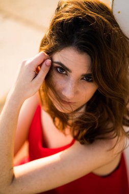 Kırmızı bluz ve altın kolye takan esmer bir mankenin yakın plan fotoğrafı. Kameraya bakıyor..