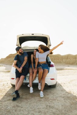 Young group of friends on a road trip sitting in a car trunck