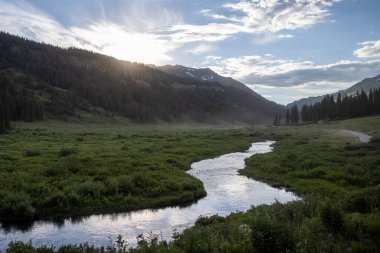 Temiz bir nehri olan güzel bir dağ manzarası. Bulutlu güzel mavi gökyüzü. Yaz fotoğrafı, ama buzullarda hala biraz kar var. Önde eski maden binaları duruyor.