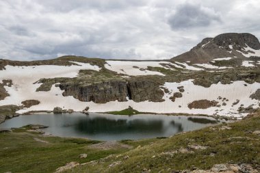 Berrak, mavi gölü olan güzel bir dağ manzarası. Bulutlu güzel mavi gökyüzü. Yaz fotoğrafı, ama buzullarda hala biraz kar var..