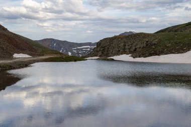 Berrak, mavi gölü olan güzel bir dağ manzarası. Bulutlu güzel mavi gökyüzü. Yaz fotoğrafı, ama buzullarda hala biraz kar var..