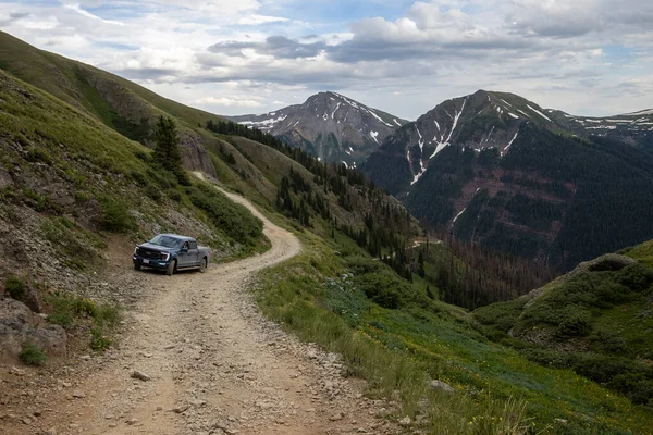 Amazing scenery. Mountain and valleys provide unbeatable natural scene. Summer colors with some snow still peaking out here and there. Blue pickup truck parked on the road