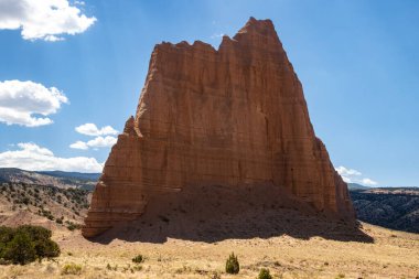 Utah, ABD 'deki Capital Reef Ulusal Parkı' nda çarpıcı kaya oluşumları. Onlara Katedral deniyor. Sarı, turuncu ve gri taşlardan yapılmış bir sürü eşsiz şekil var. Ön planda çöl bitkileri. Mavi gökyüzü.