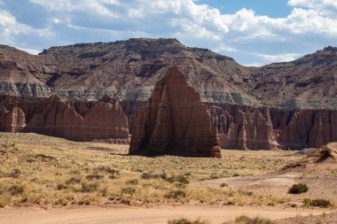 Utah, ABD 'deki Capital Reef Ulusal Parkı' nda çarpıcı kaya oluşumları. Kırmızı, turuncu ve gri taşlardan bir sürü eşsiz şekil. Ön planda çöl bitkileri. Mavi gökyüzü. 