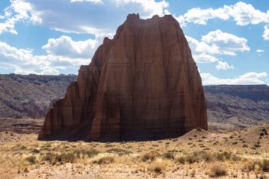 Utah, ABD 'deki Capital Reef Ulusal Parkı' nda çarpıcı kaya oluşumları. Kırmızı, turuncu ve gri taşlardan bir sürü eşsiz şekil. Ön planda çöl bitkileri. Mavi gökyüzü. 